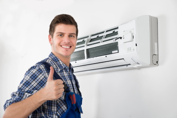 HVAC technician doing a thumbs up with the indoor unit of a ductless air conditioner