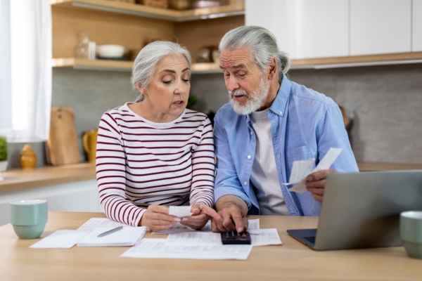 senior couple tracking heating oil usage while using calculator and checking old bills