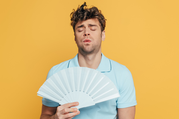 man cooling himself with a fan due to high humidity levels at home
