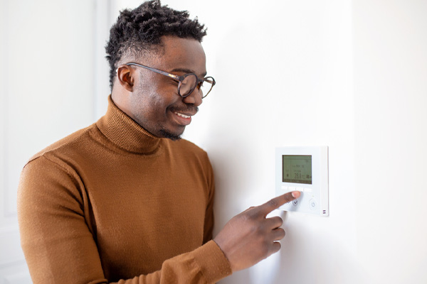 image of a homeowner adjusting thermostat due to air conditioner problems