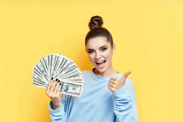 excited woman holding money on one hand and doing a thumbs up on the other hand depicting Efficient and Budget-Friendly Heating Oil Delivery
